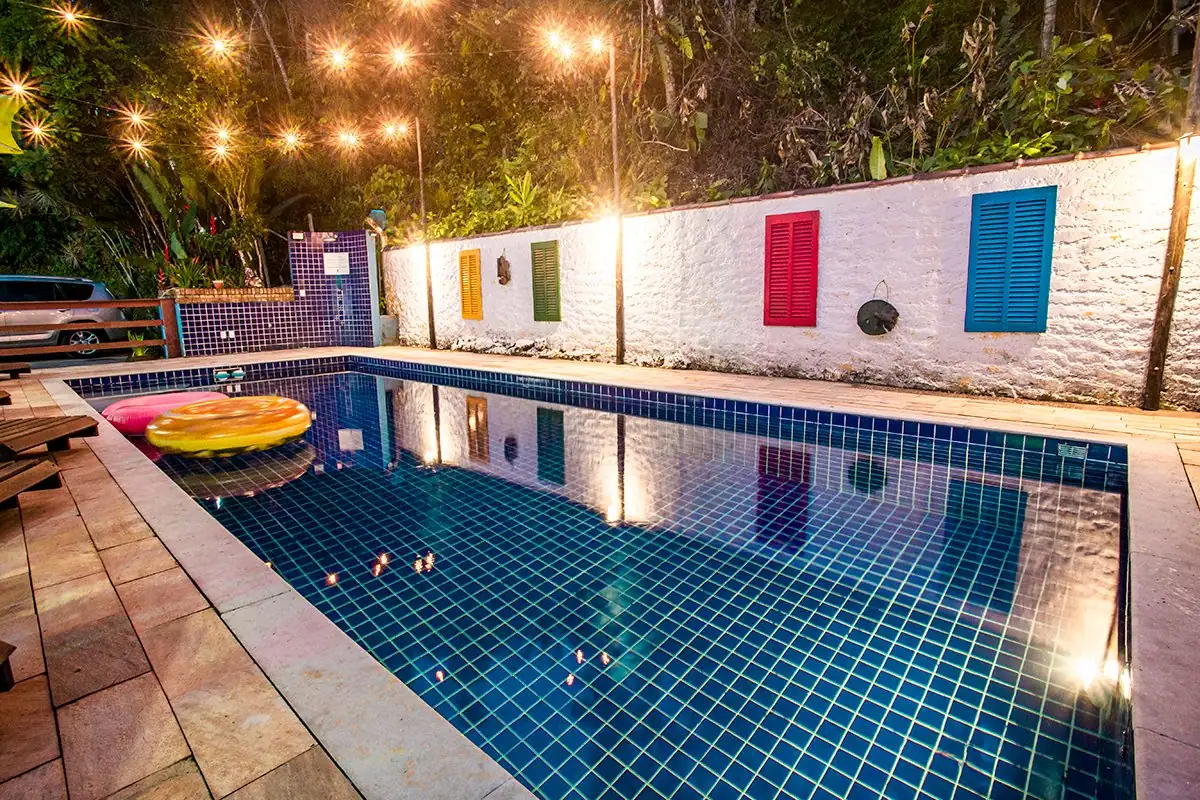 Piscina iluminada à noite, com luzes penduradas e janelas coloridas