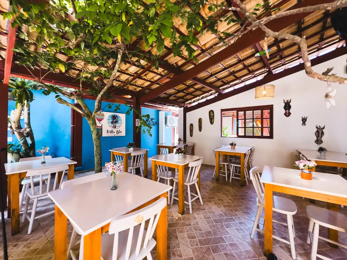 Salão do café da manhã com mesas de madeira e janelas azuis